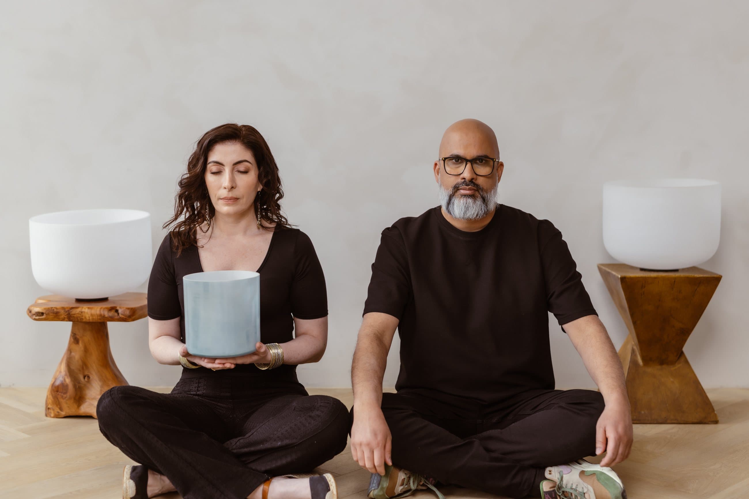 Jennifer and Steve seated on the floor between two crystal bowls, both facing forward, Jennifer holding a small blue bowl with her eyes closed
