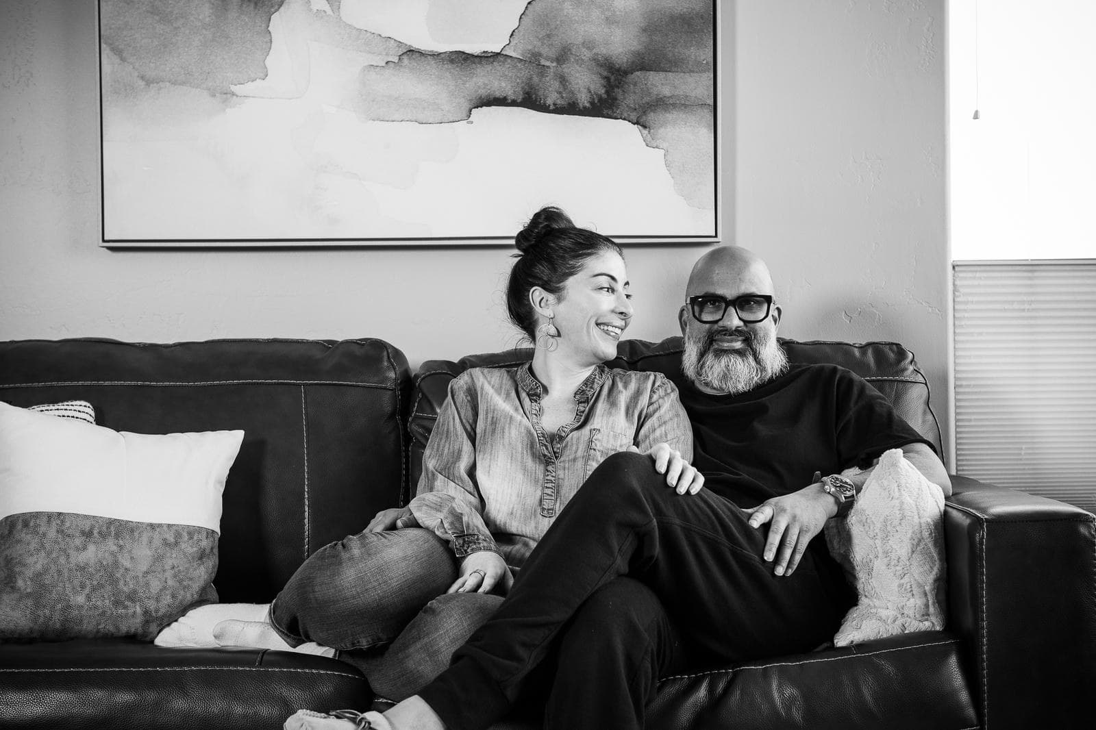 Jennifer and Steve laughing together on a sofa, in black and white
